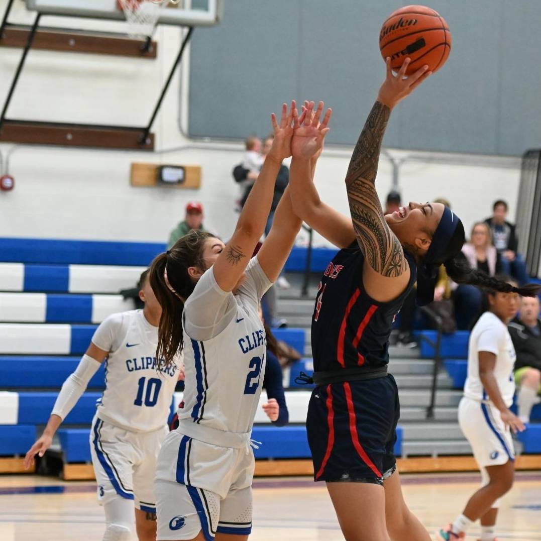 An LCC women's basketball player doing a jump shot while being blocked.