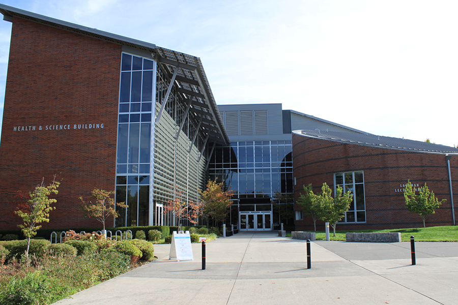 Health & Science Building Health and Science Building featuring a glass facade, landscaped entrance, and surrounding trees in a clear sky setting.