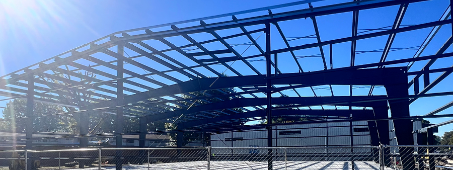 Construction of indoor sporting facility showing the flooring structure and metal inner structure. Sunny skies and blue background with a construction fence around the build.
