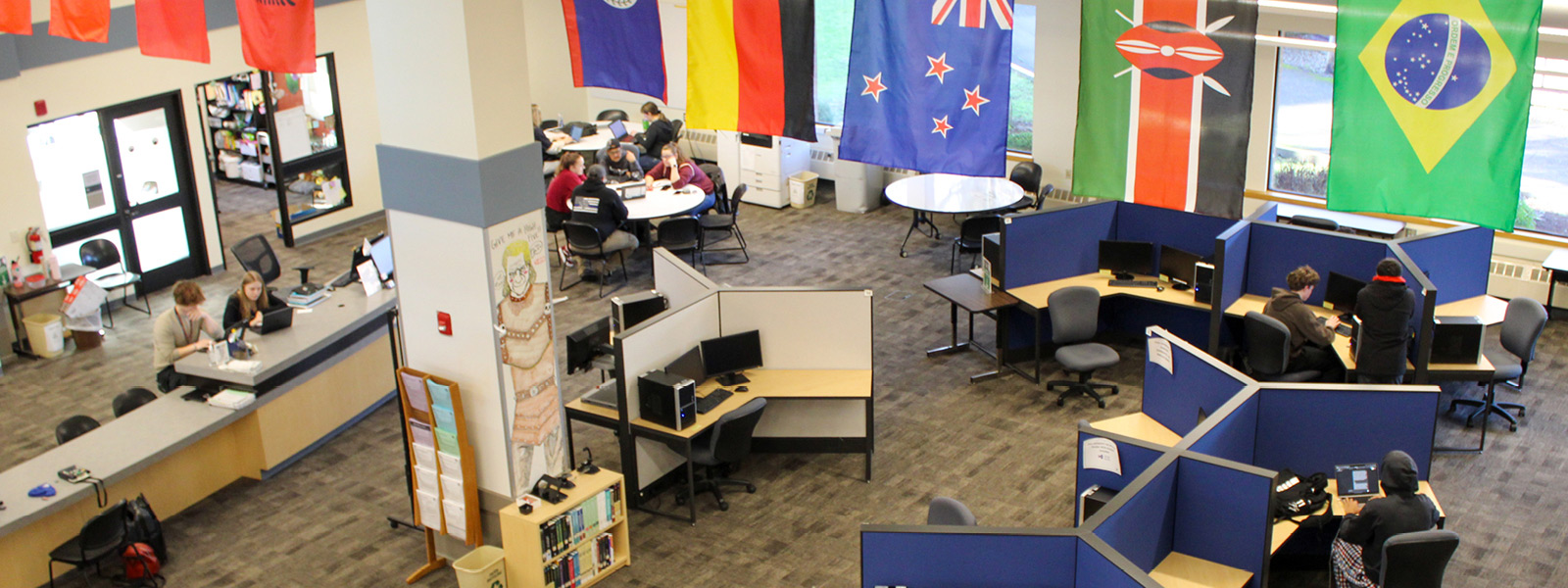 A spacious study area with students working at desks, surrounded by international flags hanging from the ceiling.