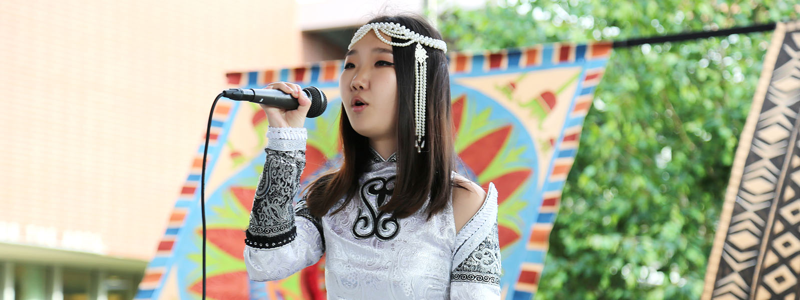 Asian female wearing decorative/celebratory white dress and headband, standing and singing with a microphone