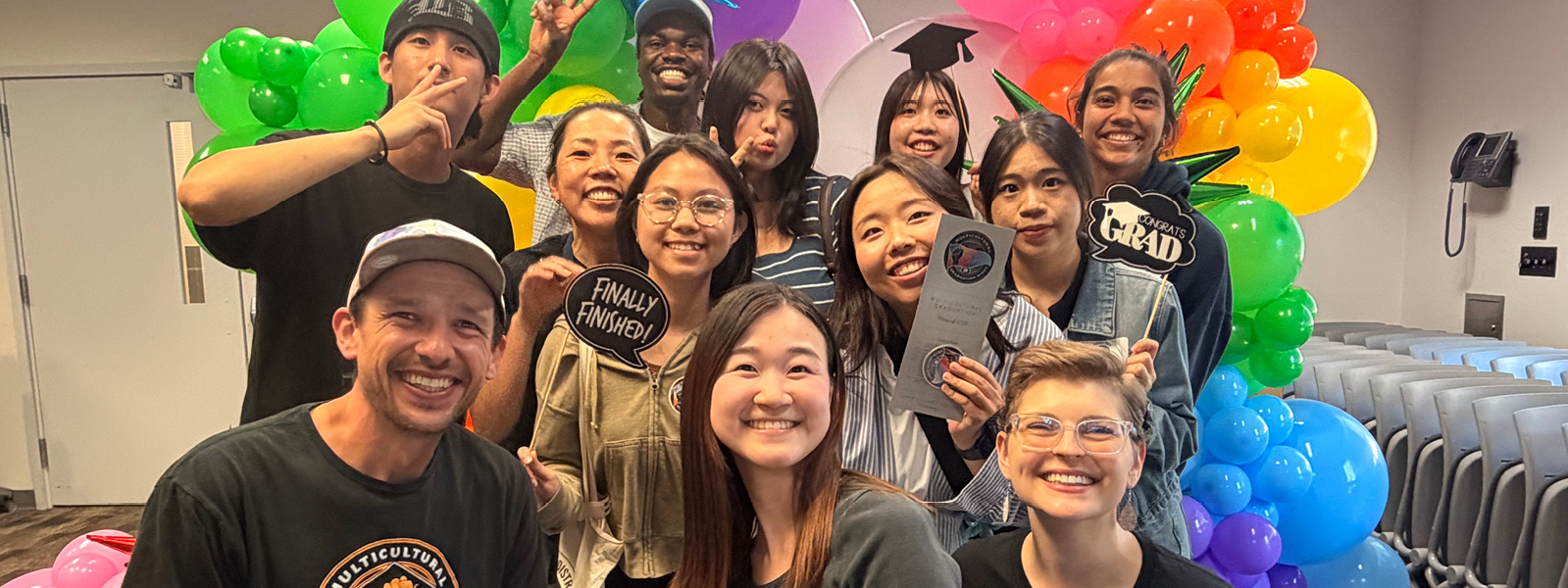 Group of International students and their advisor smiling at at photo booth with colorful baloons in the background