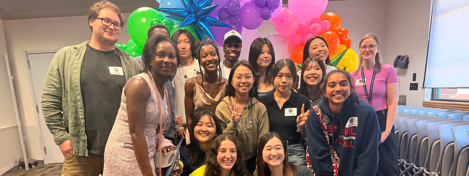 Large group of Multiculteral students holding "congrats Grad" signs in front of a multicolor balloon arch photo booth