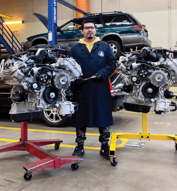 photo of Vidal Villagran in auto shop next to two engines