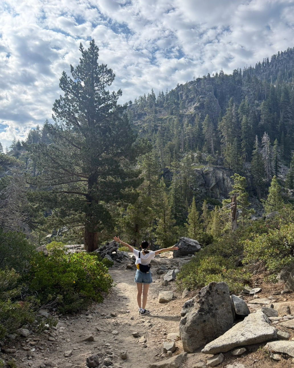 A girl wearing a t-shirt and shorts with her back to the camera as she poses with her arms out stretched, with a mountain in front of her