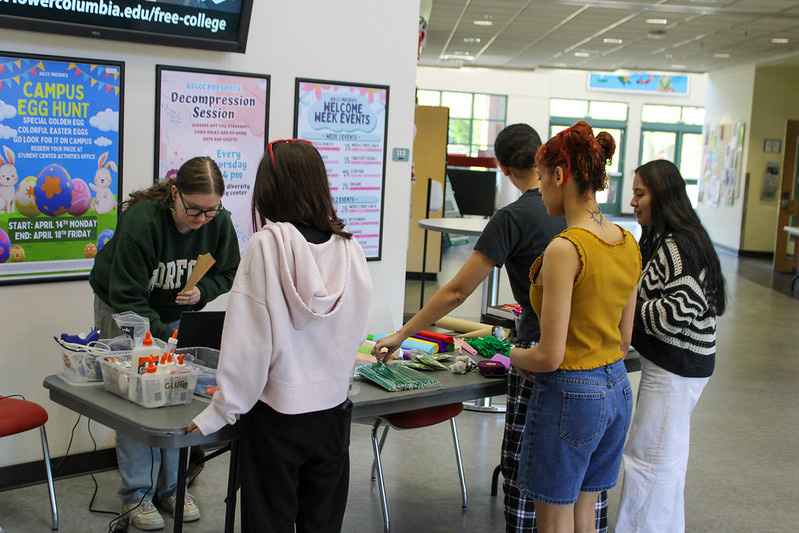 DIY Paper Flowers Students Gathering around a table with craft paper, pipe cleaners, pompoms and other supplies to make paper flowers