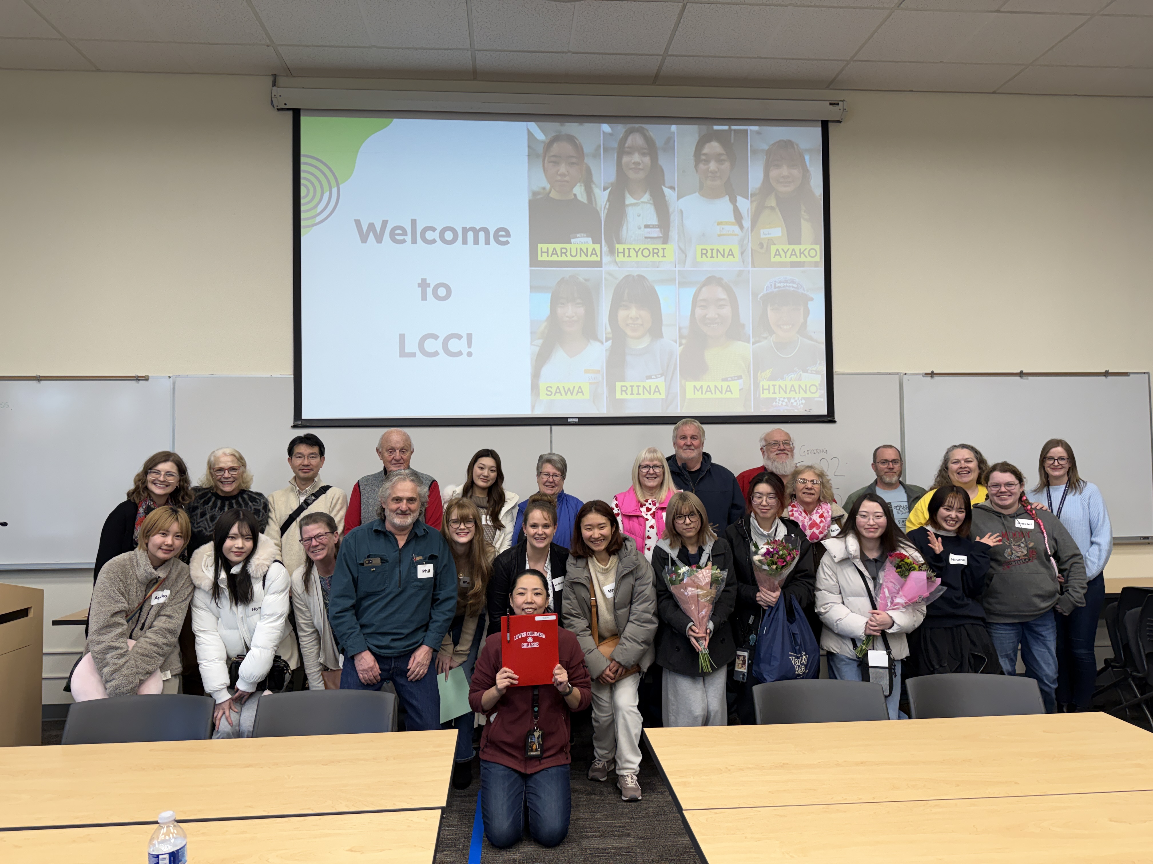 Group photo of international students, faculty, and staff at lower columbia college in from of a slide show that says "Welcome to LCC"