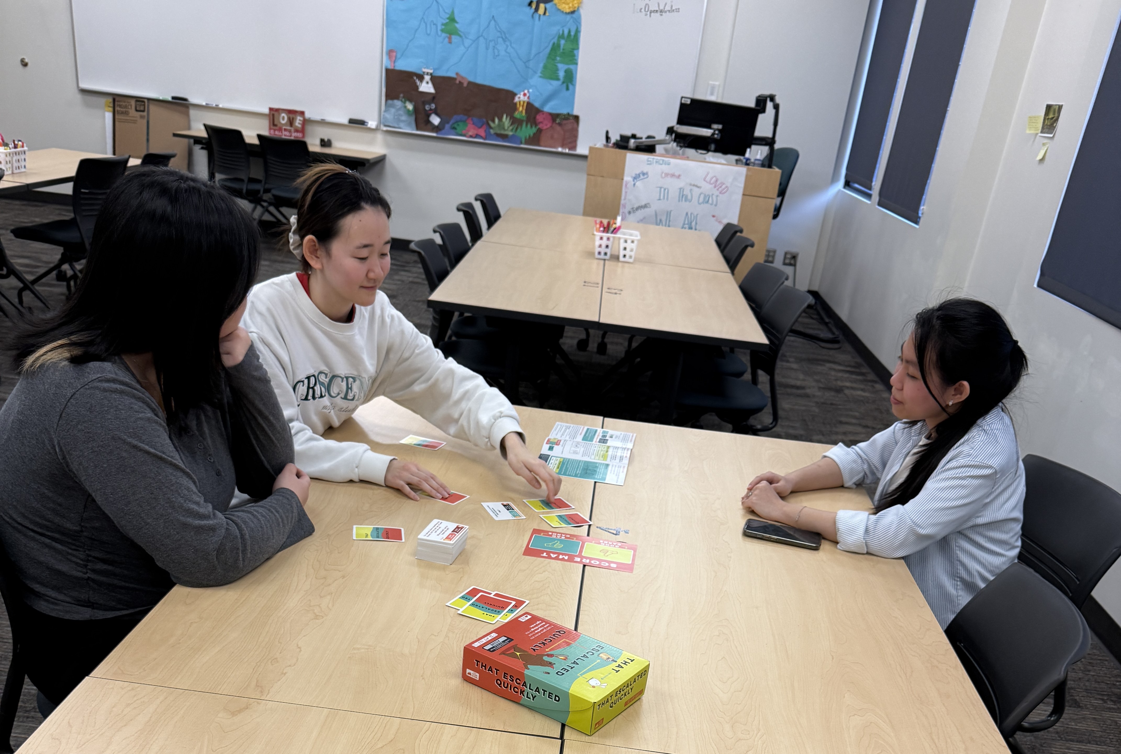 Three International students sitting at a classroom table playing card games