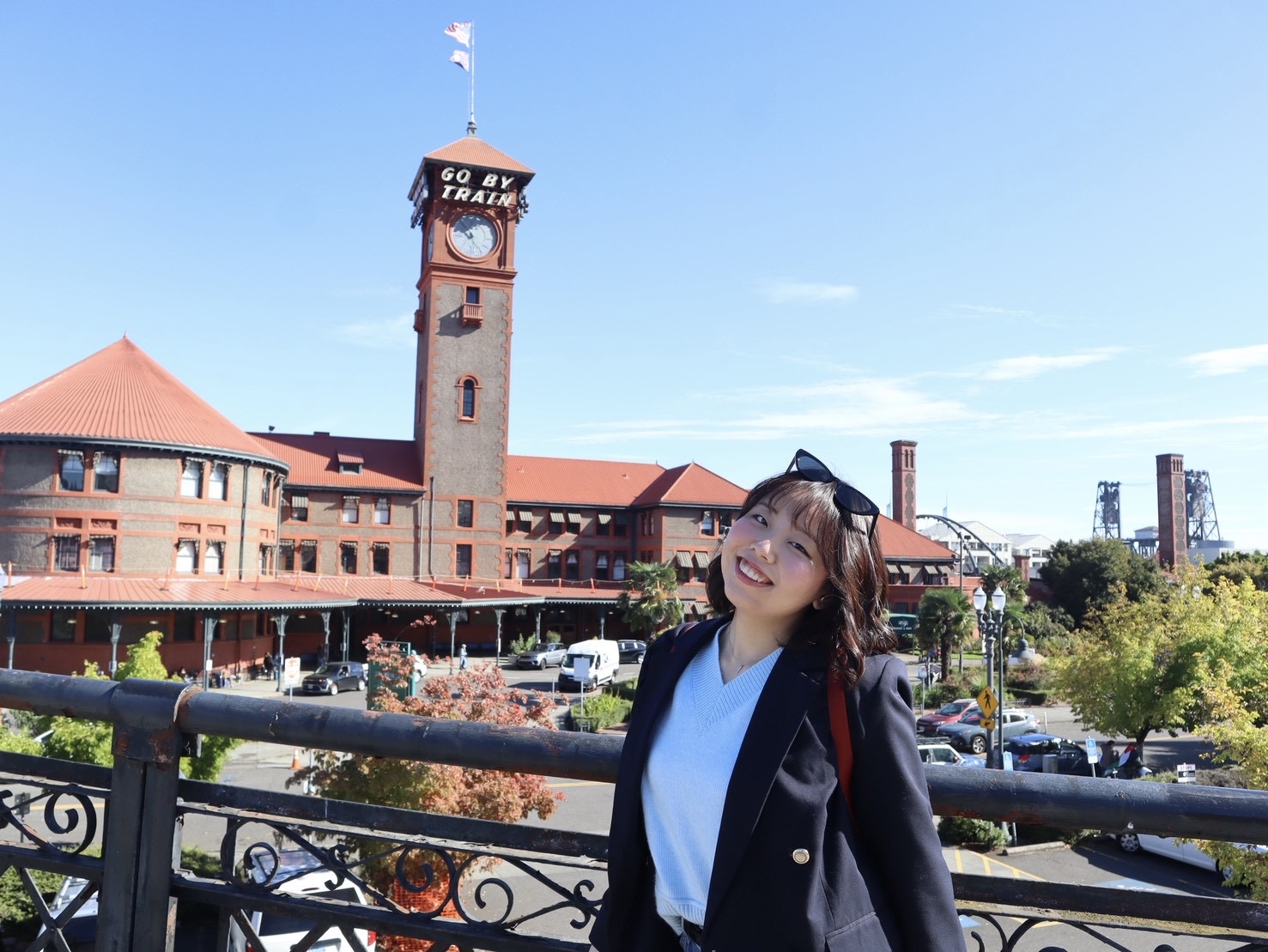 International Student Ariso smiling and posing for a photo on a sunny day with city landscape behind her