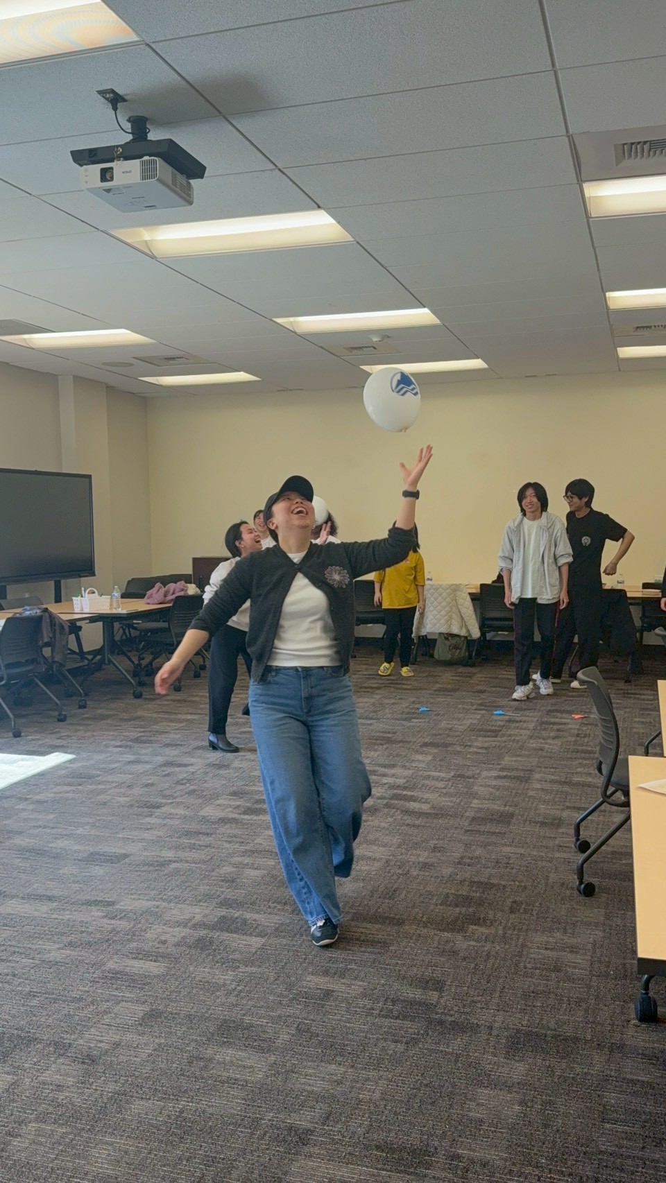 International students walking across the room smiling while trying to keep their balloon in the air.