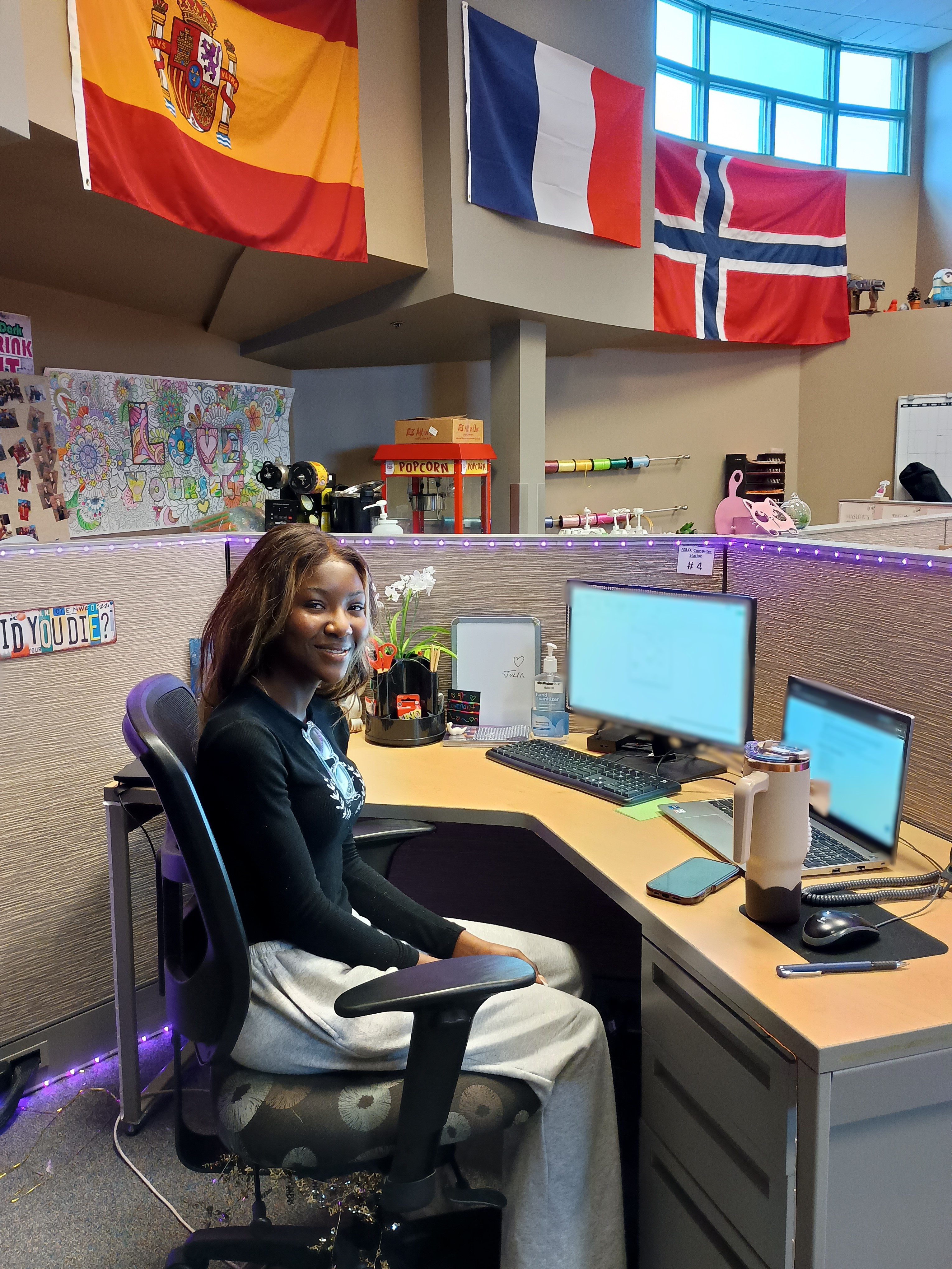 Student worker sitting in a campus building at a work desk smiling 