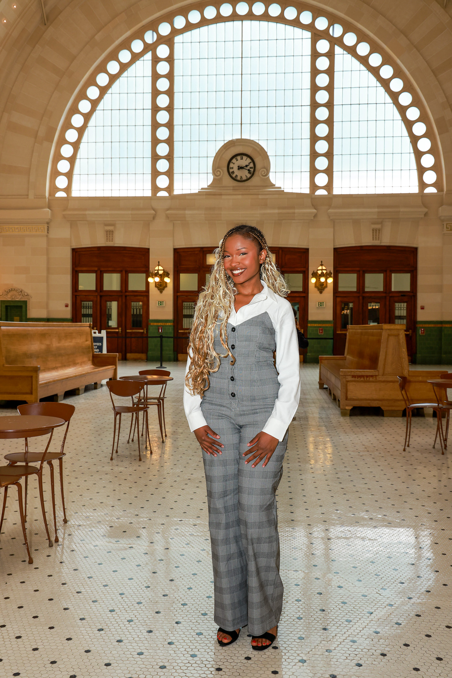 Divaa Divaa posing in an older building with a large half-circle window and wooden benches behind her