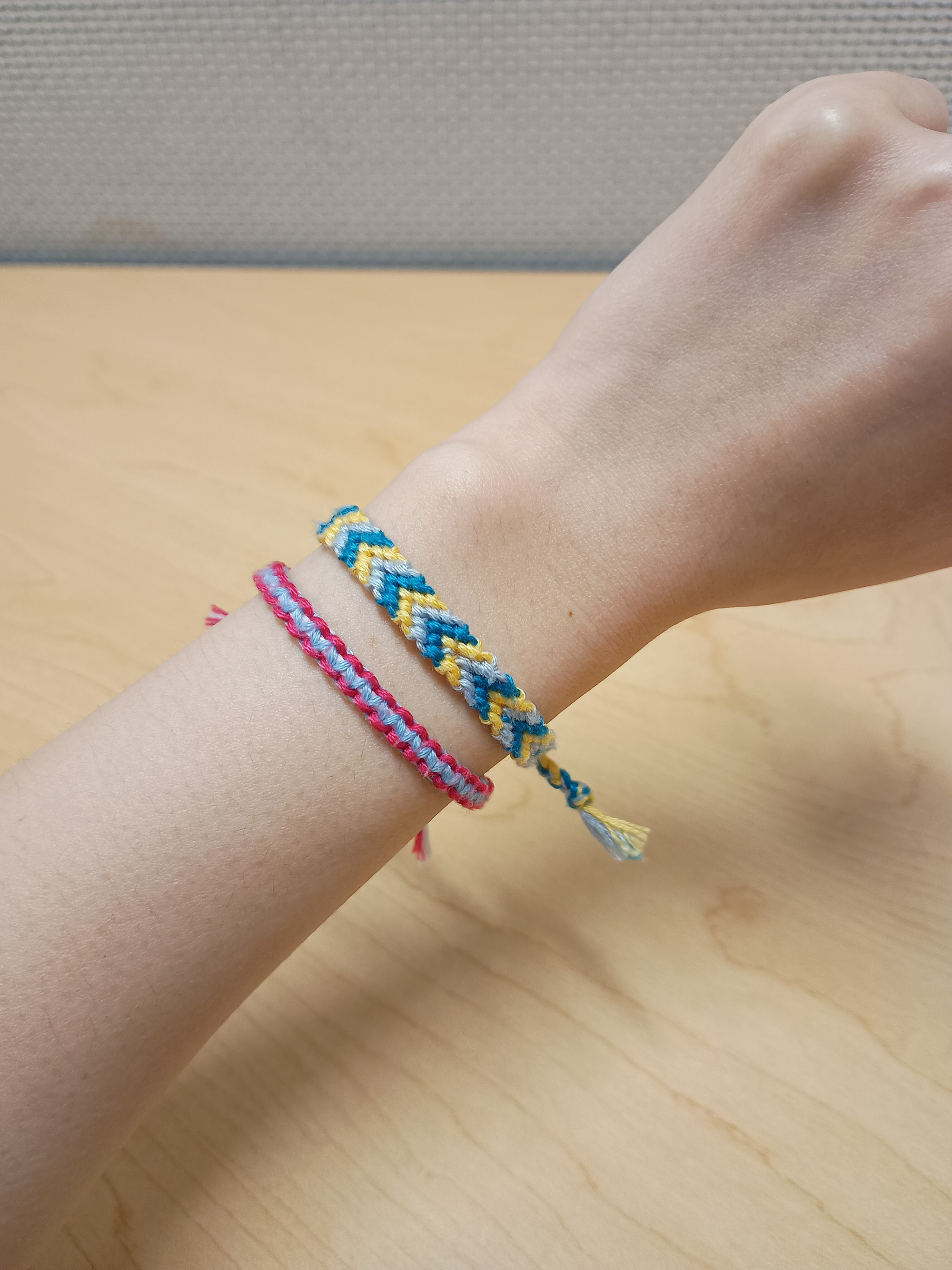 a small pink and and blue friendship braclet and a yellow, blue, and light blue striped friendship braclet