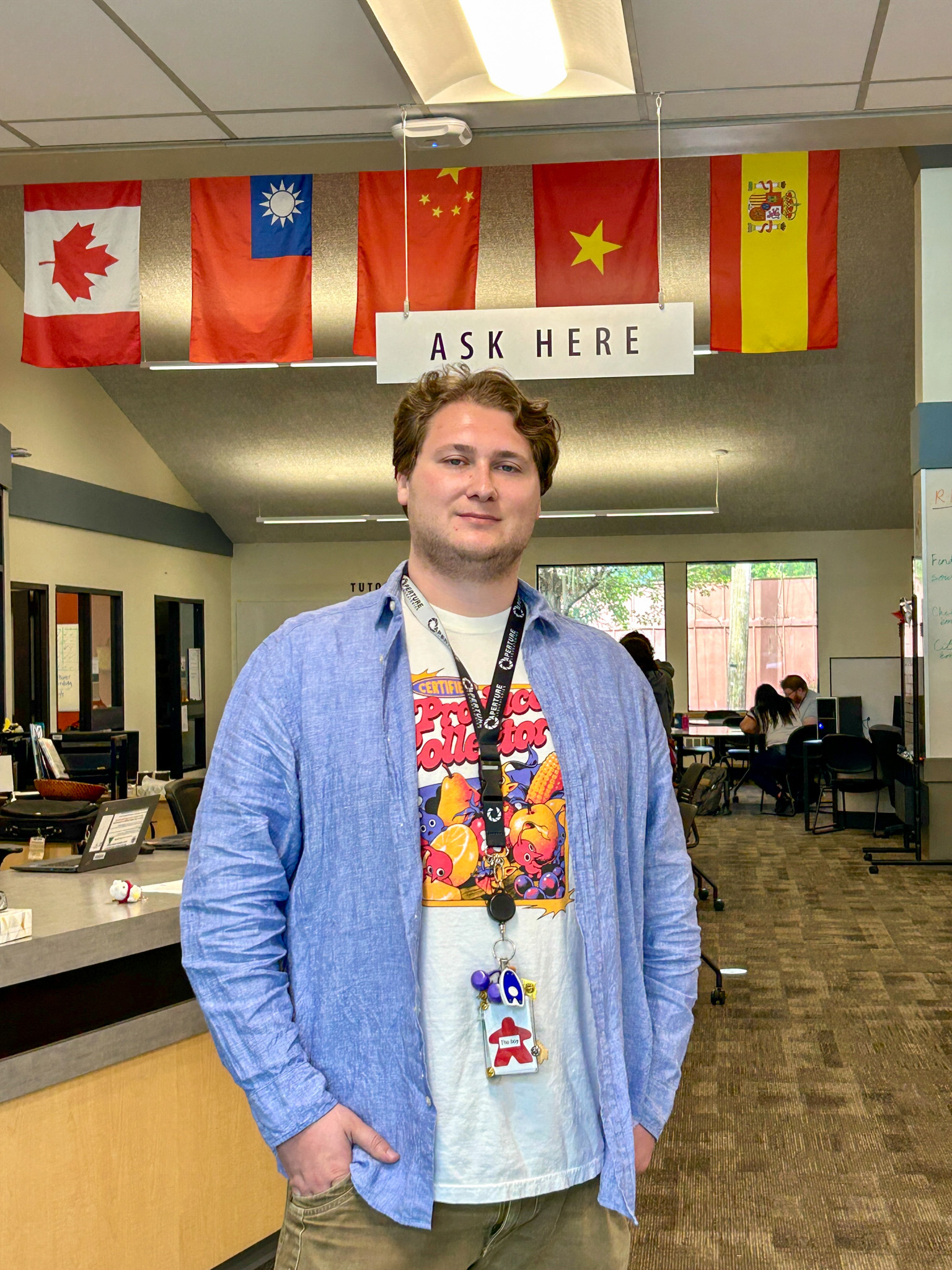 Grant Grant, a LCC student, stands at the library's "Ask Here" desk beneath a row of international flags.