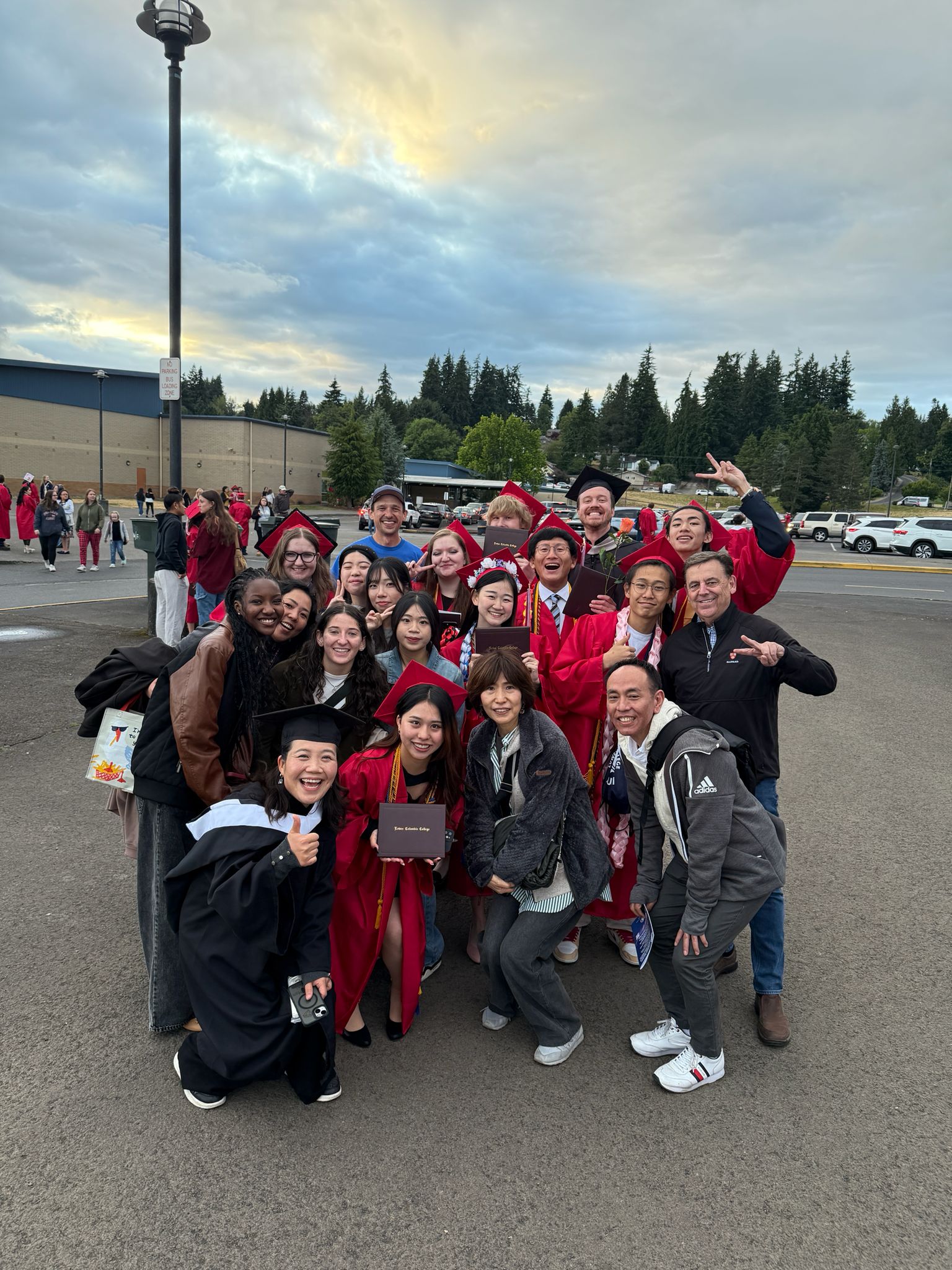 Group Photo of international students at the Lower Columbia College Graduation. Kelso High school in the background and students are wear red cap and gowns.