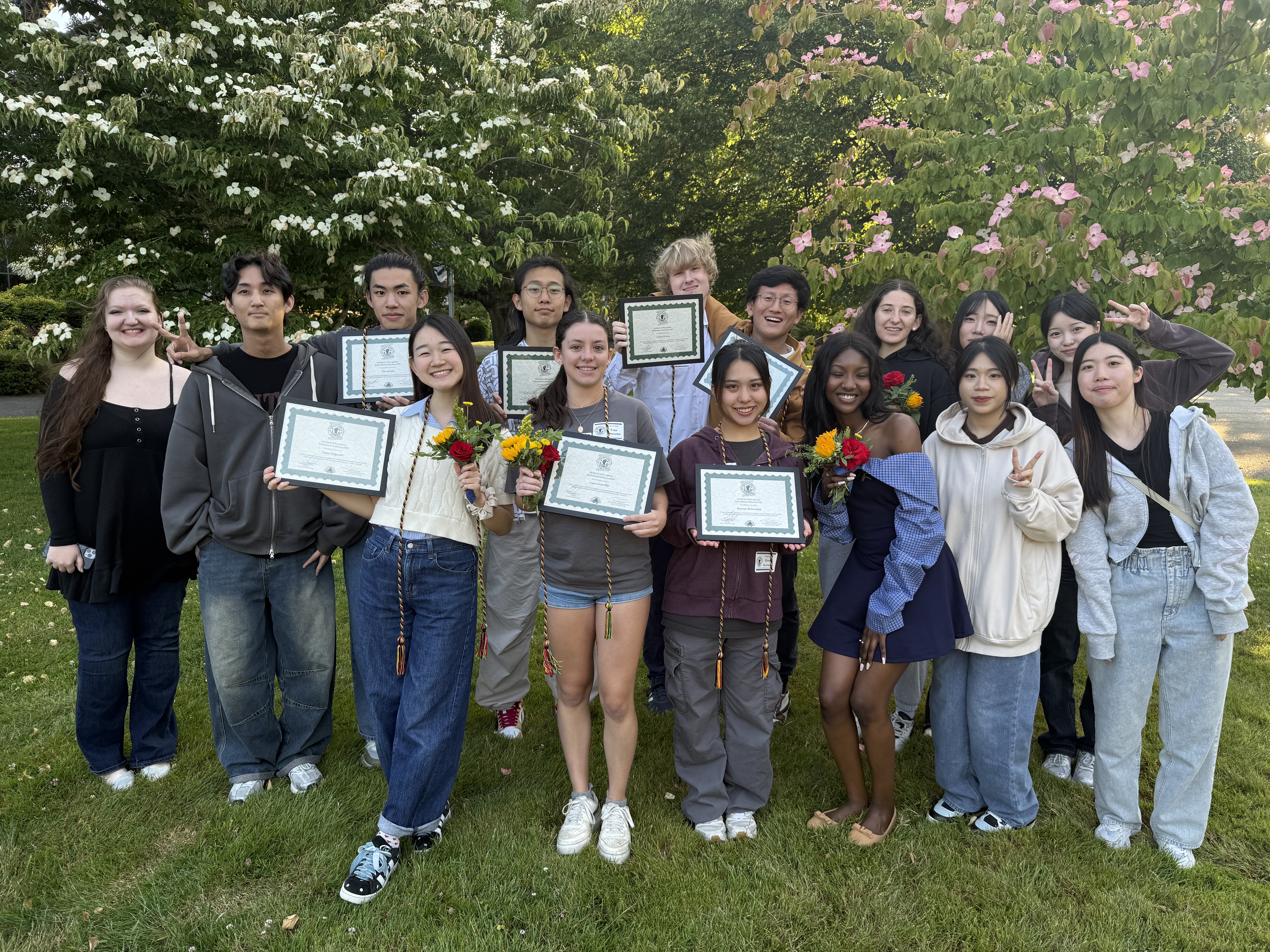 International Program Students taking a group photo with college awards from Multicultural night with spring bloom and trees behind them