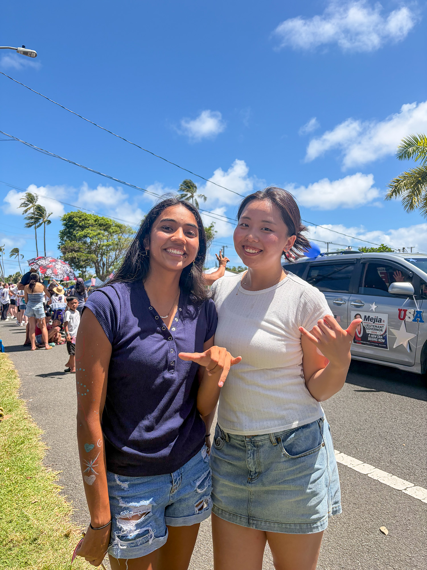 Hawaii-Arisa with her friend 2 girls standing on the edge of the street as a parade passes behind them