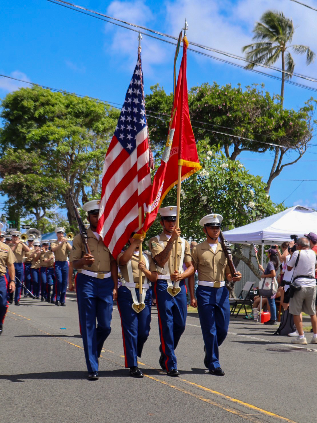 Hawaii-Parade 1 4 soldiers marching side by side the two in the middle are carrying flags and the two on the outside are carrying rifles