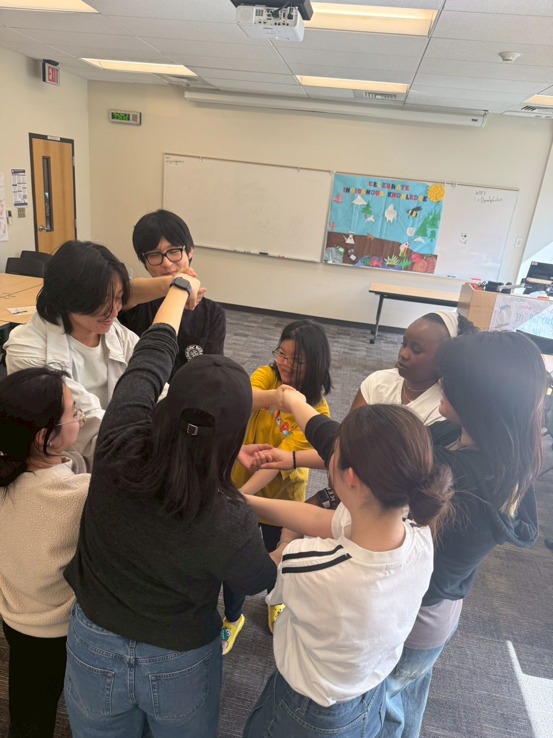 International students in a circle in a campus classroom playing the human knot