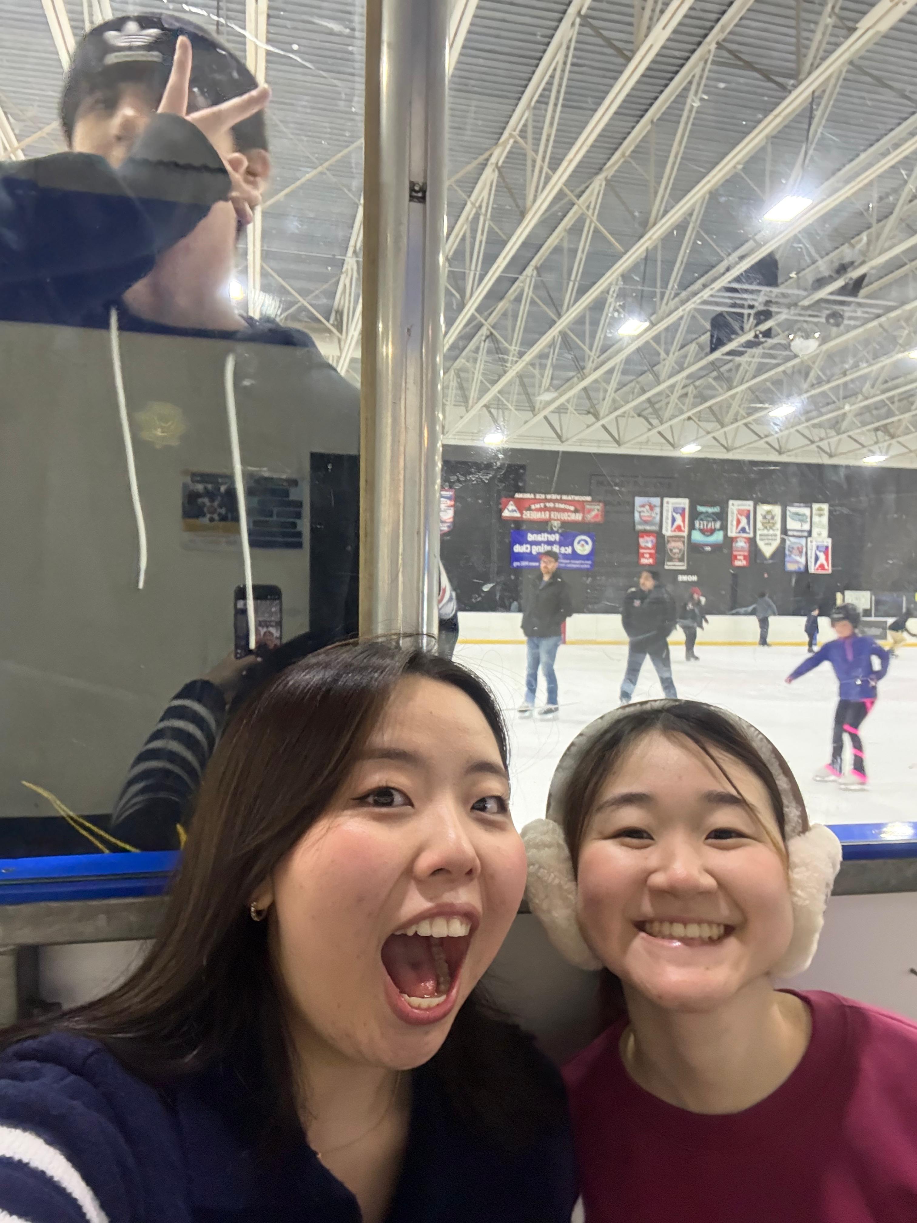 Two students smile for a selfie at an ice skating rink.