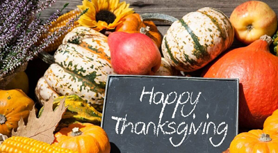 Happy thanksgiving sign sitting on top of a pil of colorful squash, corn and sunflowers