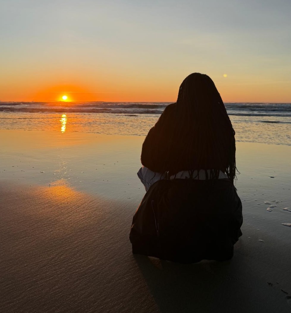 Students sitting on the wet sand watching the dusk sunset at the beach