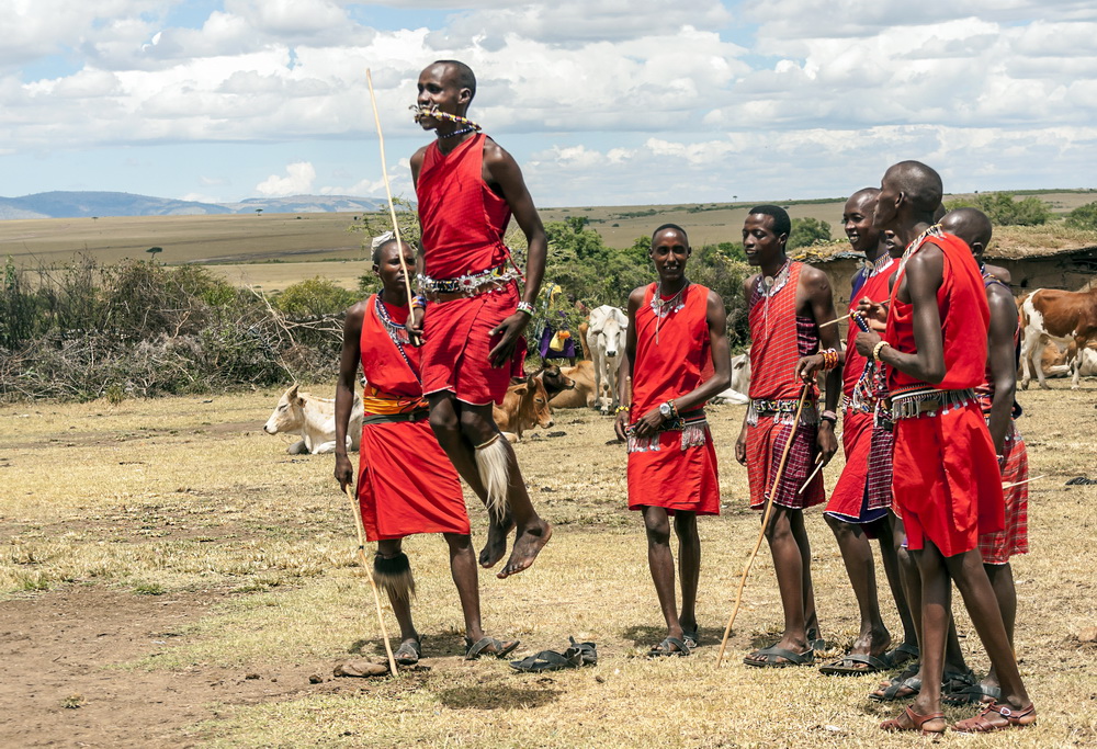 Kenyan men in red robes and walking sticks performing the Masai jump to showcase their warriors.