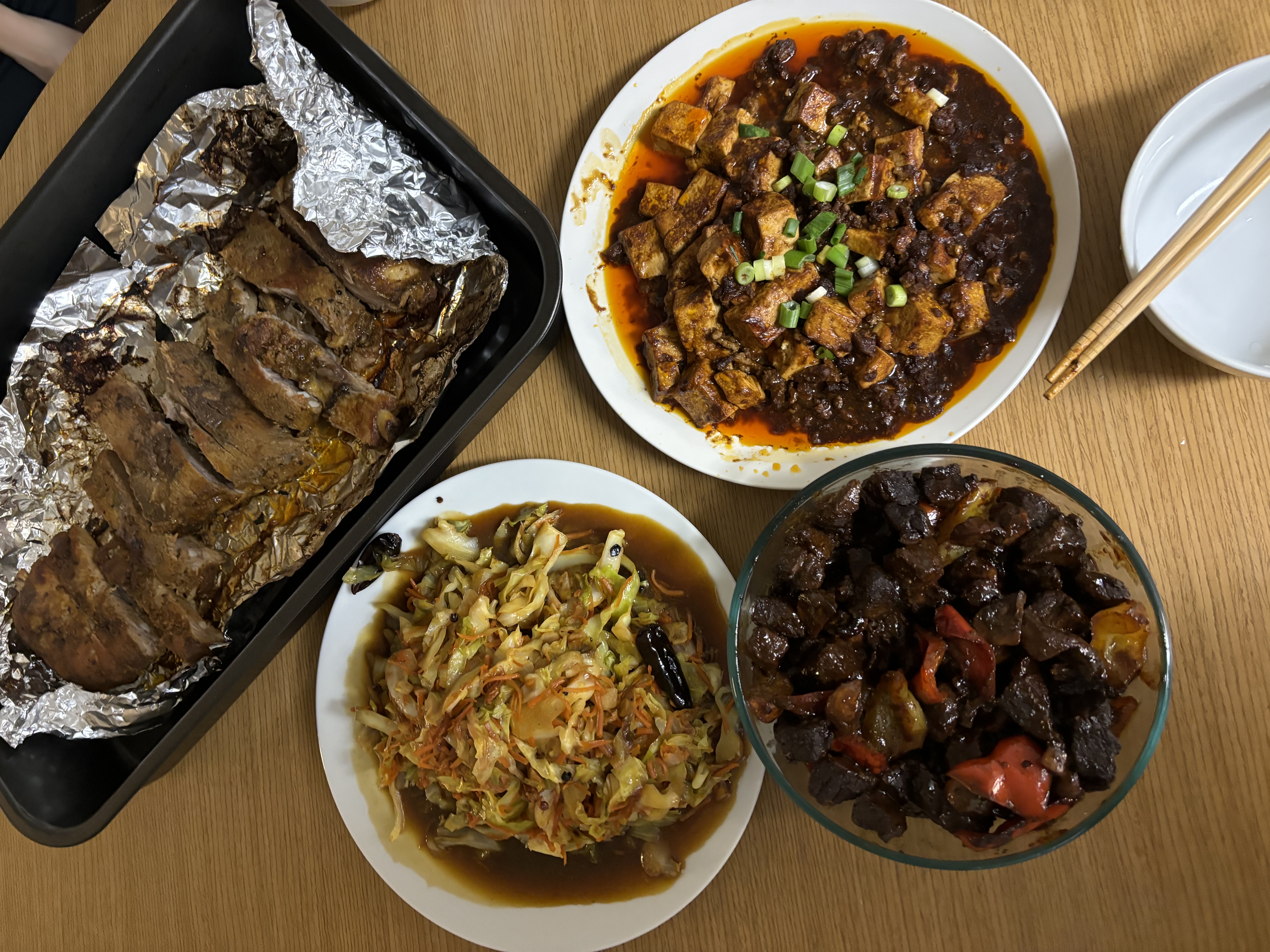 three bowls of Asain food and a pan of meat in foil.