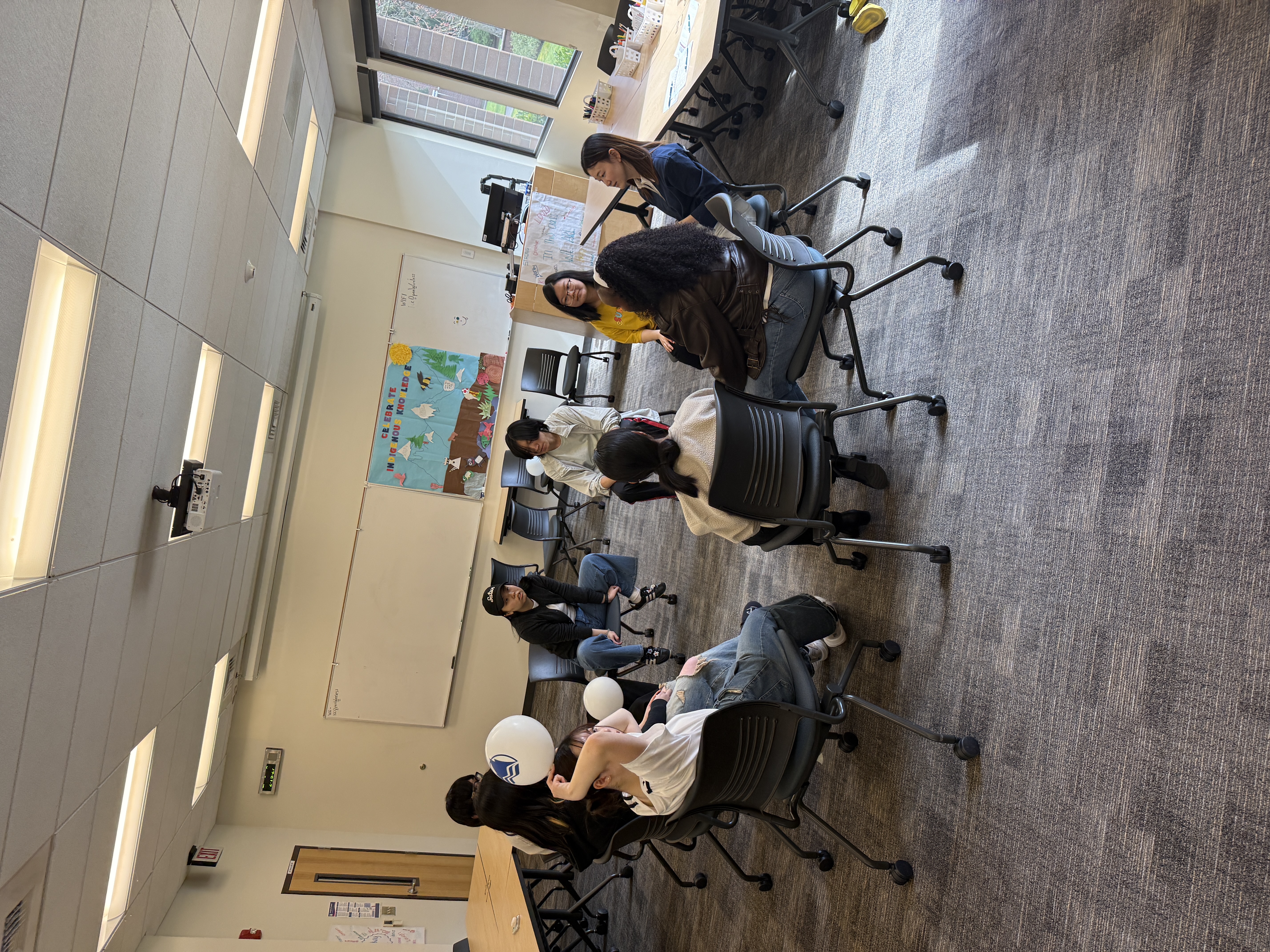 International students in a college campus room sitting in a circle in computer chairs passing a balloon around the circle