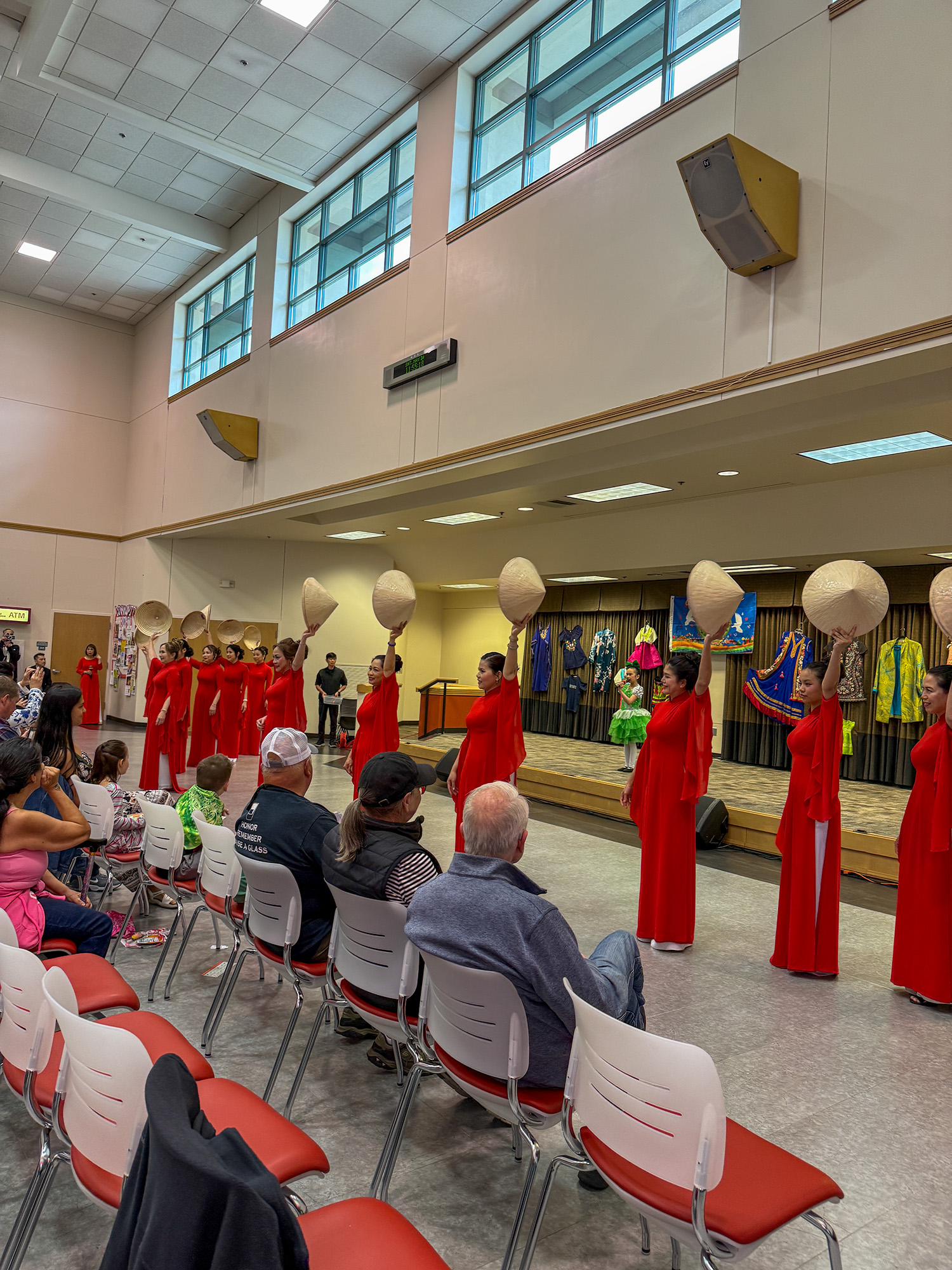 a group of performers in matching red traditional outfits and conical hats (nón lá) performing a synchronized traditional vietnamese dance routine on a stage