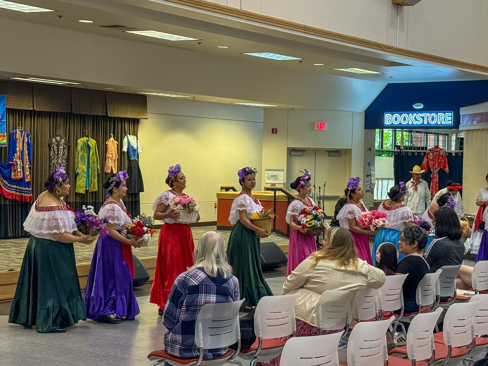 traditional Ballet Folklórico dancers in vibrant, colorful dresses,  The performers wear classic ruffled white blouses, floral hairpieces, and wide, flowing skirts in deep green, purple, and red hues