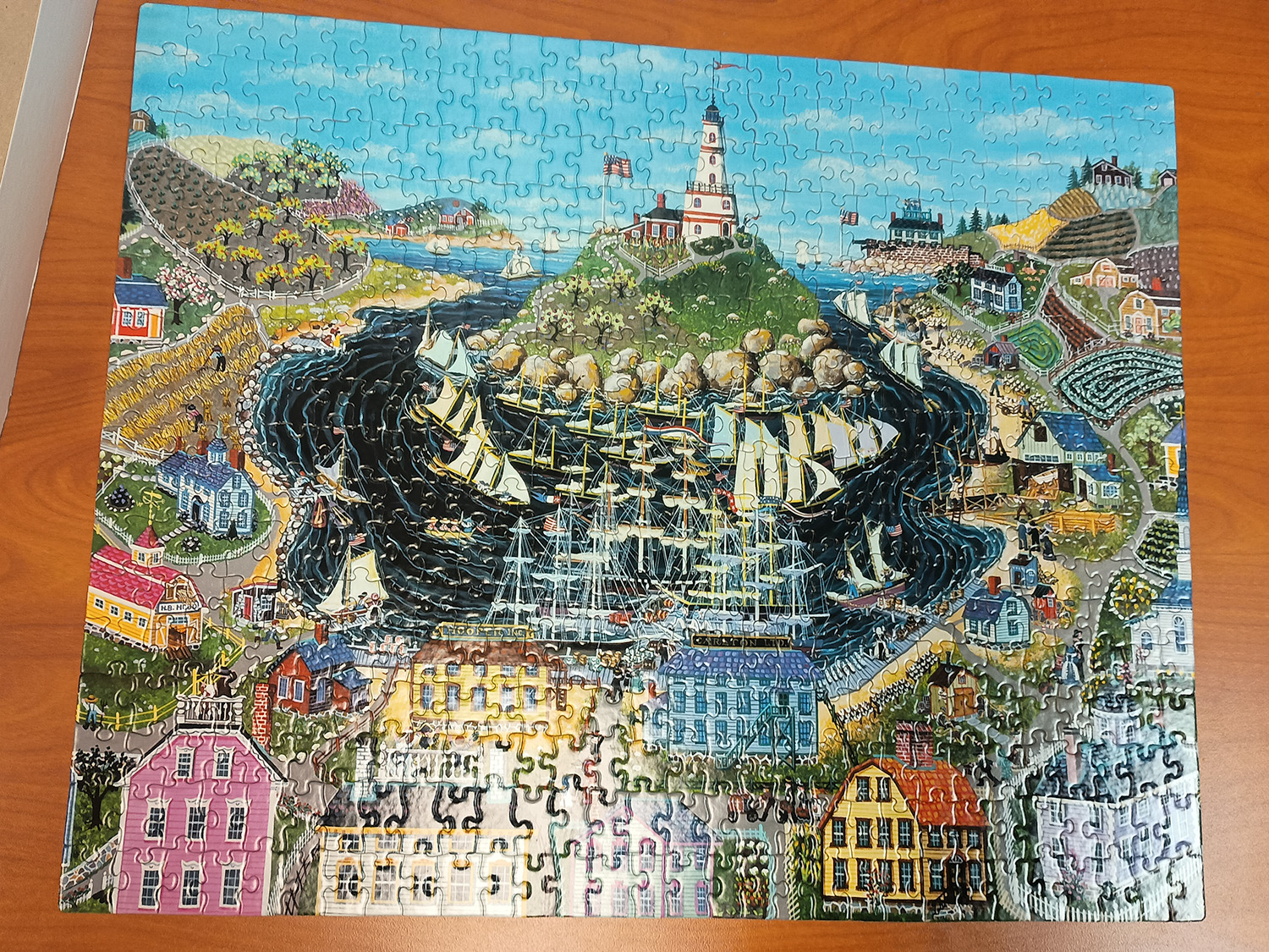 a large compleated puzzle depicting a brightly colored coastal town with a light house in the middle on an island