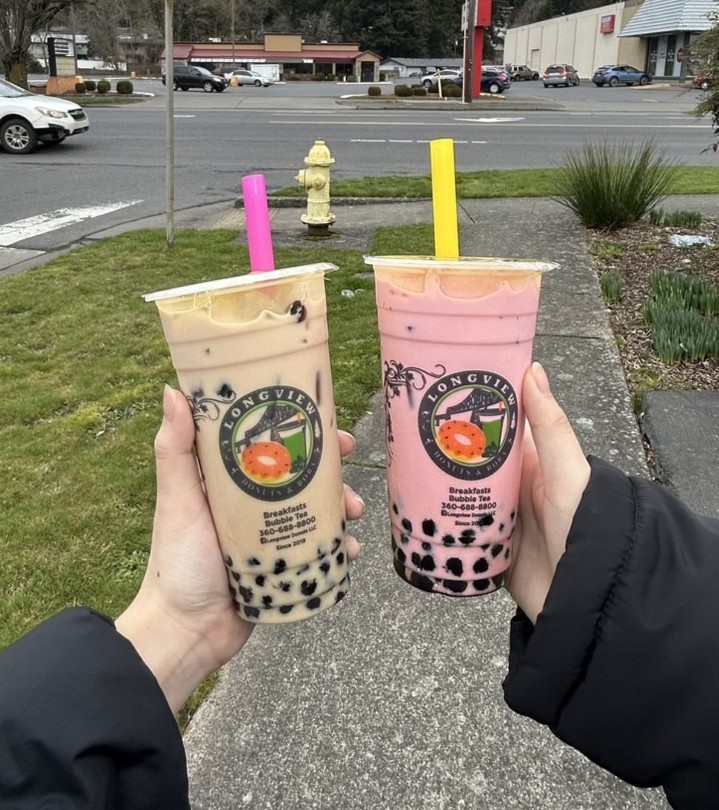 a pink and tan colored Boba tea drink being held out by two students