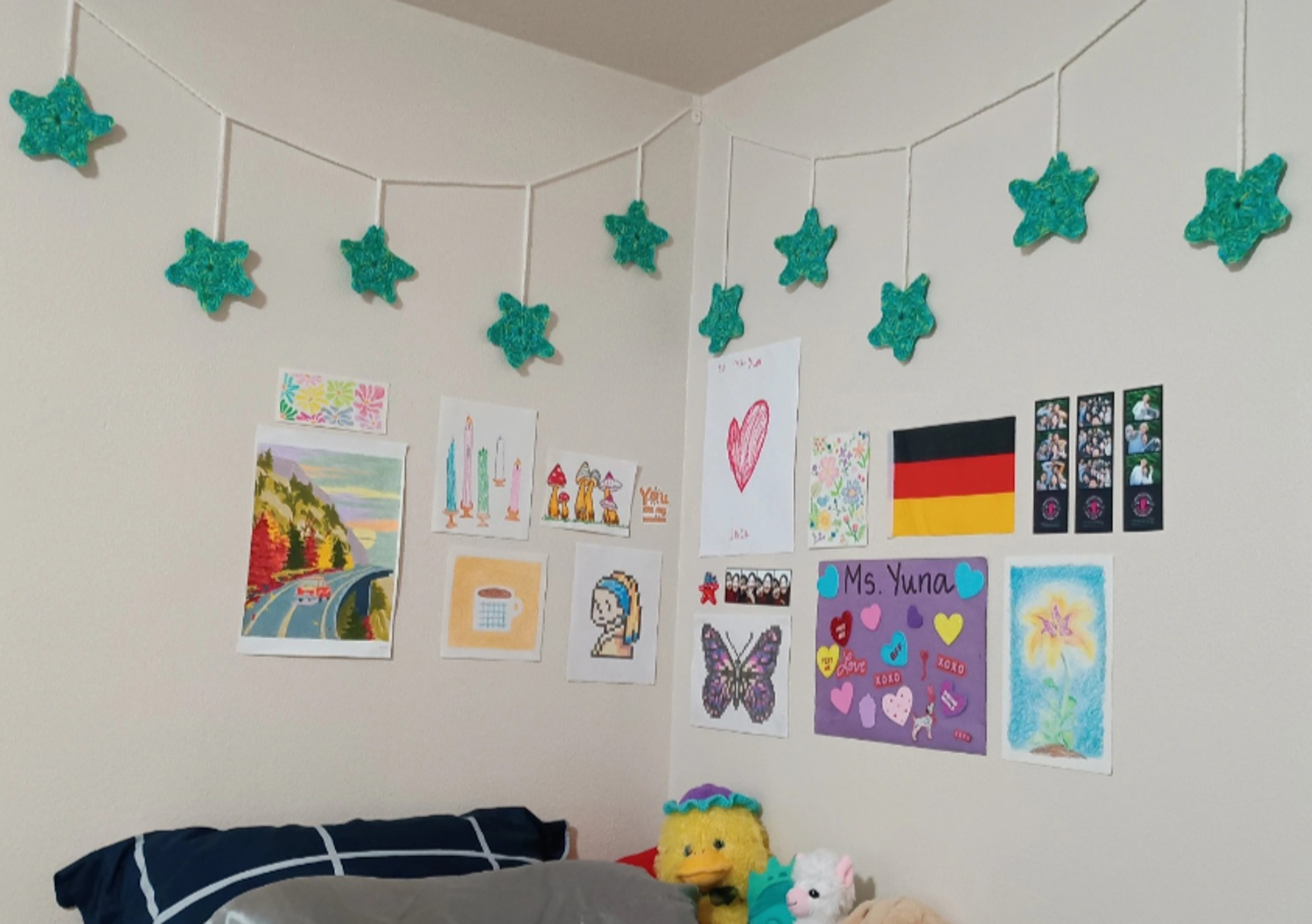 A white wall decorated with handmade drawings and green crocheted stars