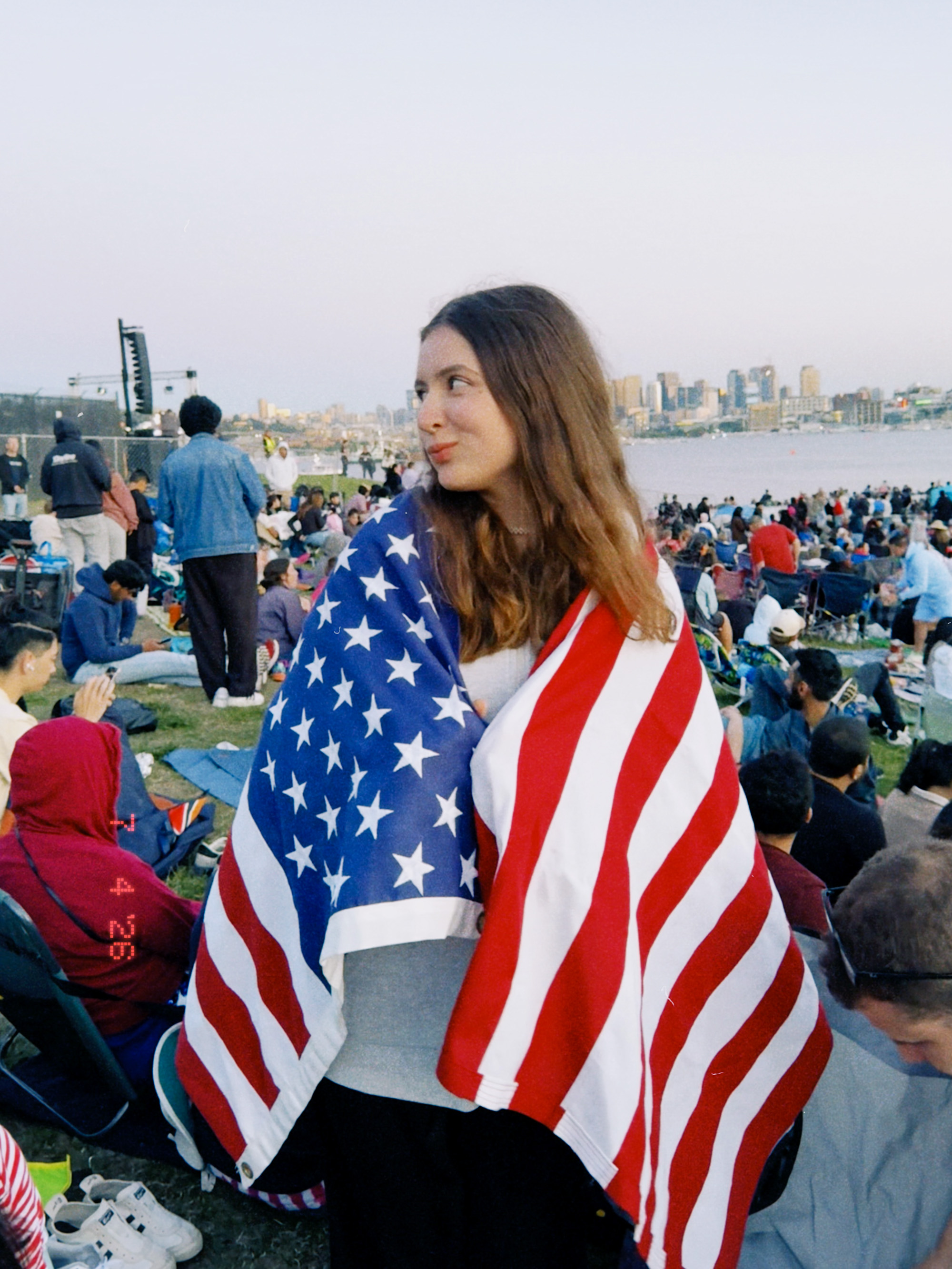 Seattle-Ania with the US flag Ania standing with a U.S. flag wrapped around her in a crowd with the seattle skyline in the background
