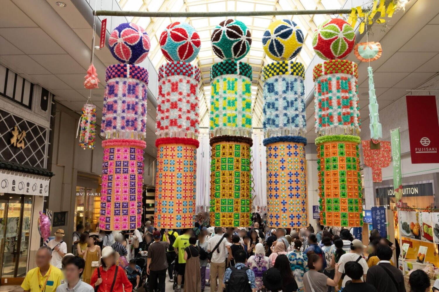 Five colorful hanging lanterns with intricate patterns hang above a group of people at the Sendai Tanbata festival. 
