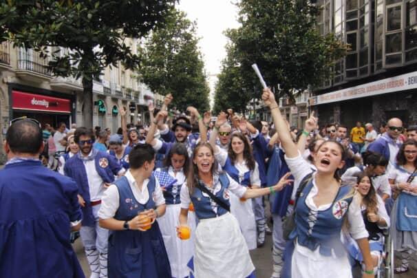 A group of women in white and blue school uniform walking down the streets cheering and smiling