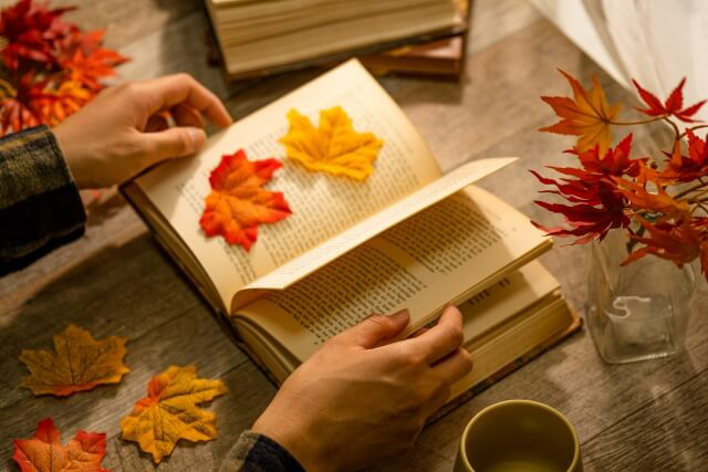 The Autumn of Reading A person holidng a book open with a orange leaf and yellow leaf sitting on one of the pages