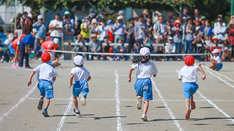 The Autumn of Sports 4 small kids running full speed in a race heading towards cheering parents and peers