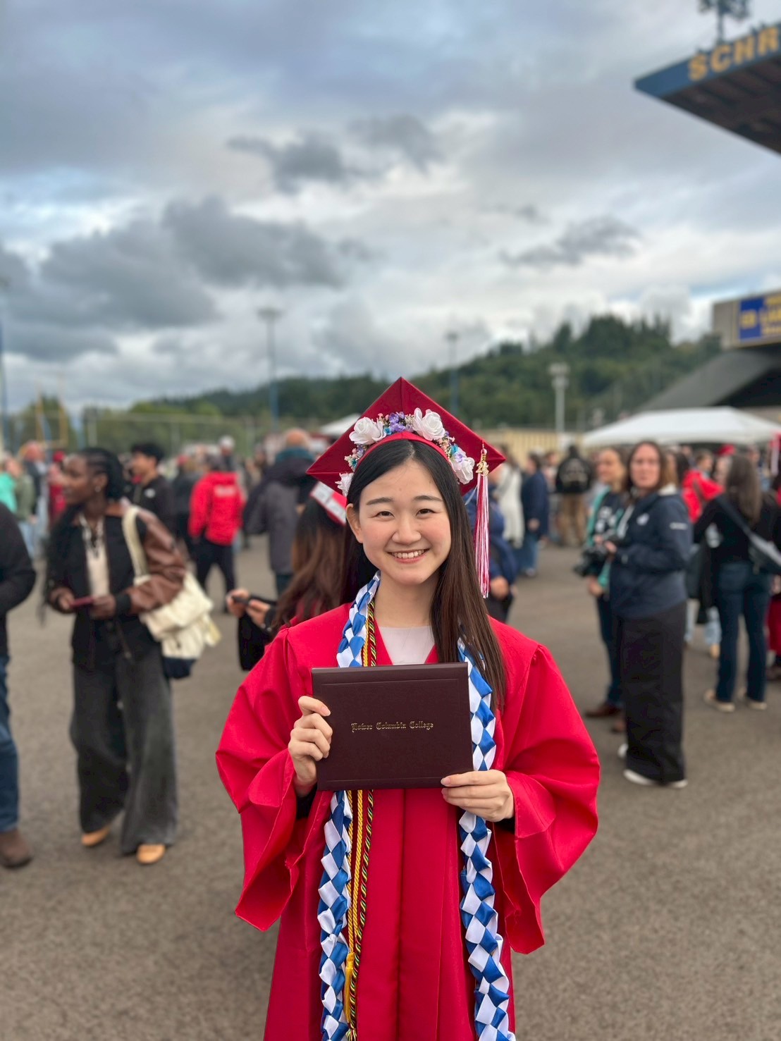 international student in red cap and gown, smiling and holder her diploma