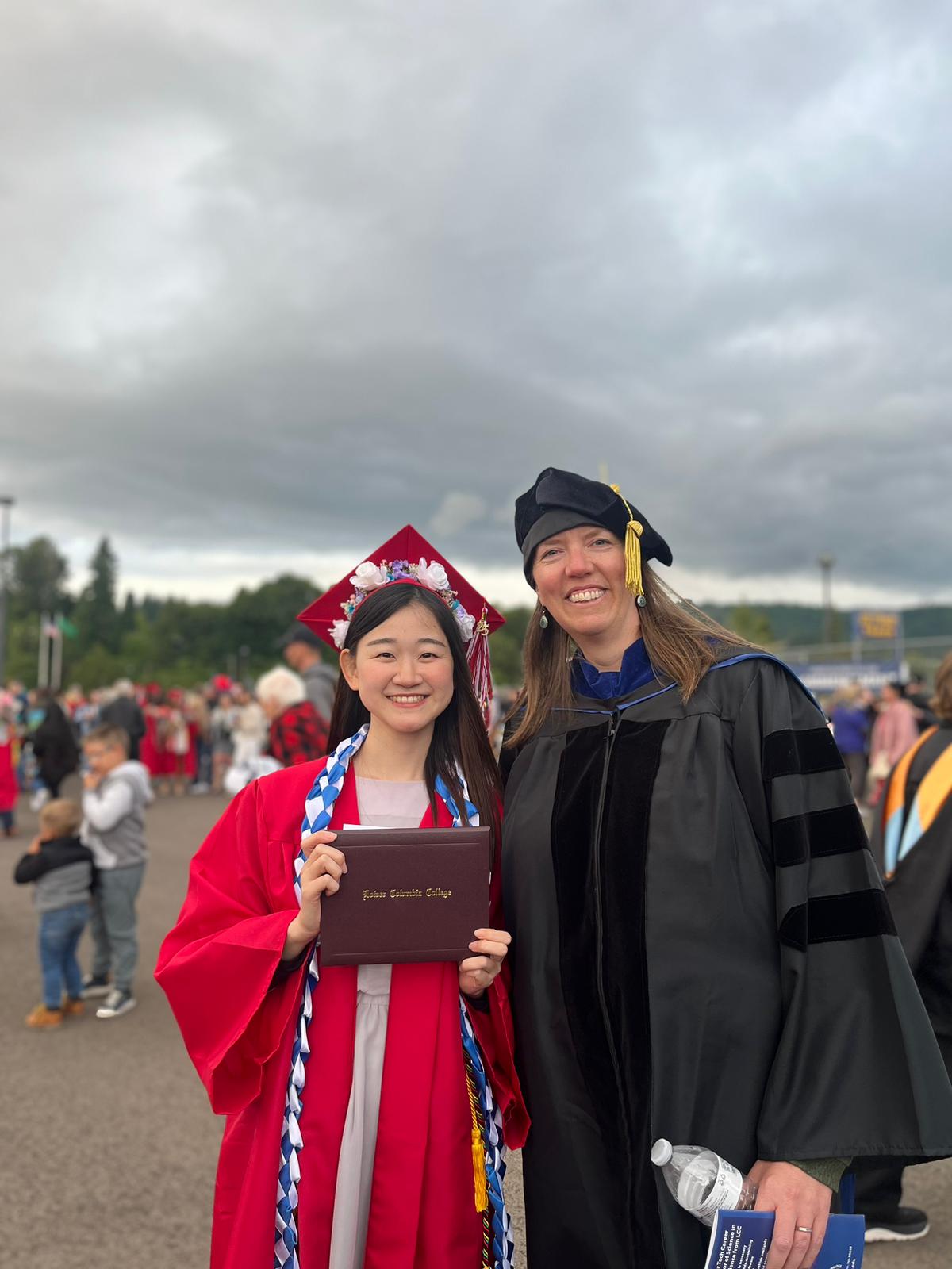 International student in red cap and gown with a teacher in graduation gown and cap