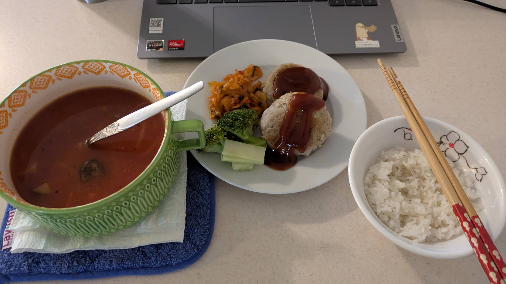 Yus meal including a soup, rive with chopsticks and a plate of assorted foods next to a students laptop