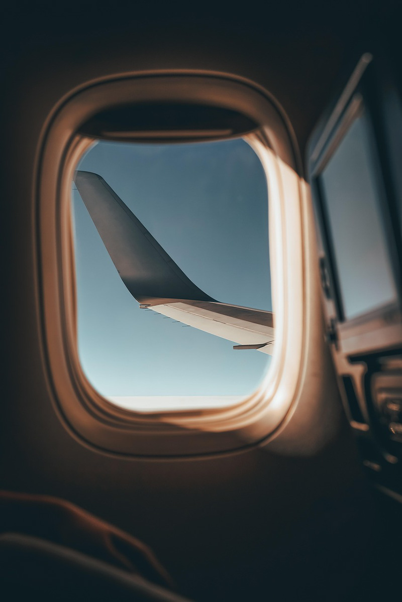 Airplane window An oval airplane window showing clear blue sky and a plane wing out side the window.