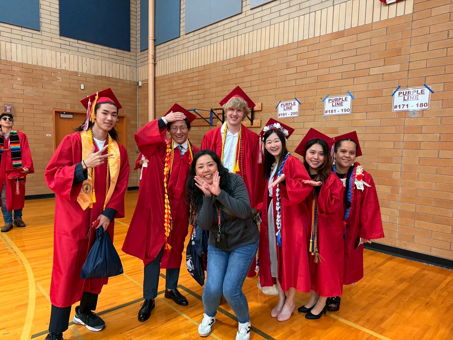 international students in their red cap and gowns standing with their college representive smiling at the camera