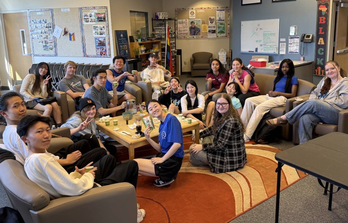 group picture of students sitting around a coffee table on campus with ceremonial team making supplies on the coffee table in the middle of the group