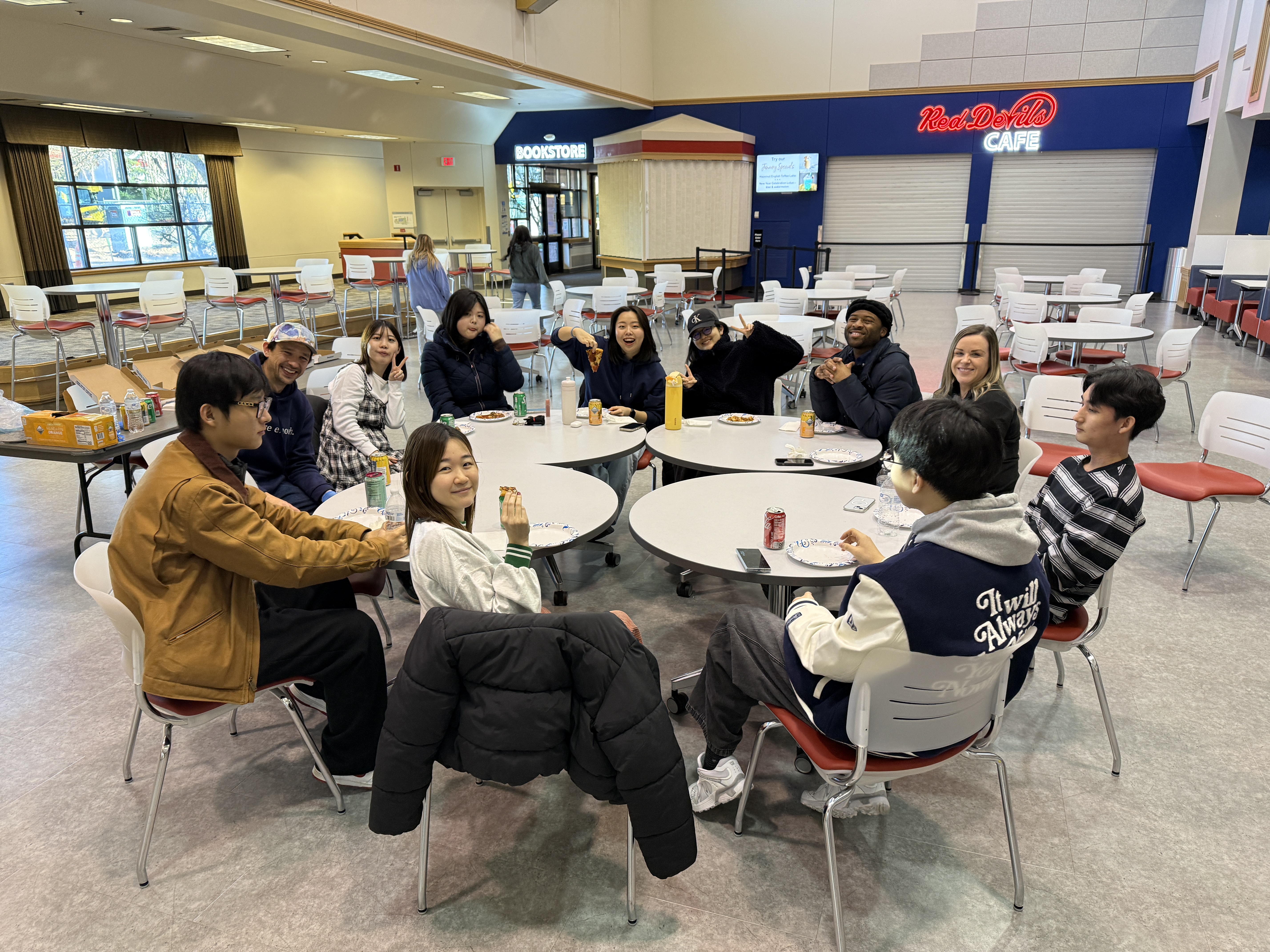 A group of international students sitting in the Lower Columbia College Student Center Cafeteria with 4 small round tables pushed together as a group and empty plates on the table
