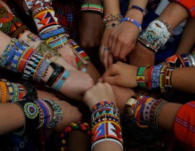 a circle of wrists and arms together displaying a colorful collection of bracelets and beads.