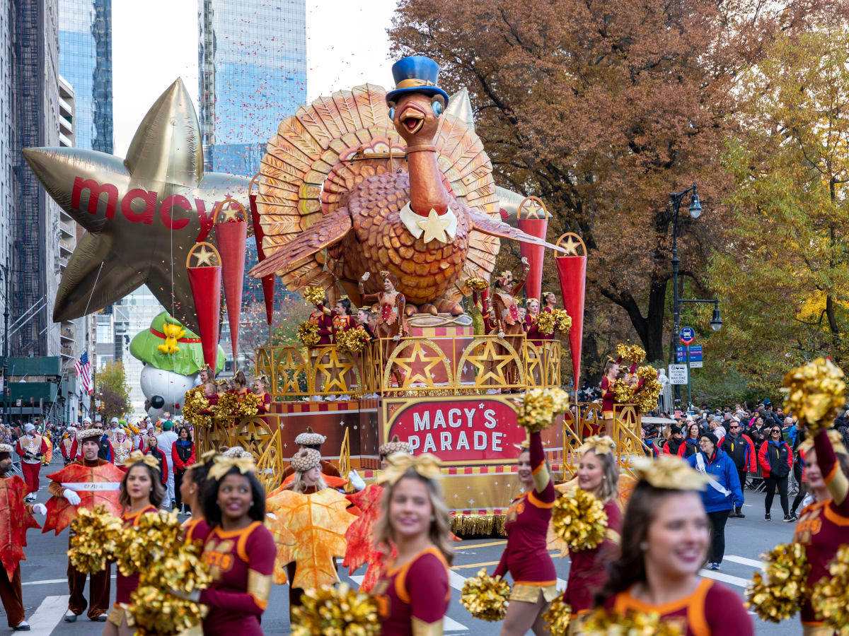 Macy Day Parade of a giant turkey wearing a top hat and large macy baloons. Community members around the sidewalks watching the parade