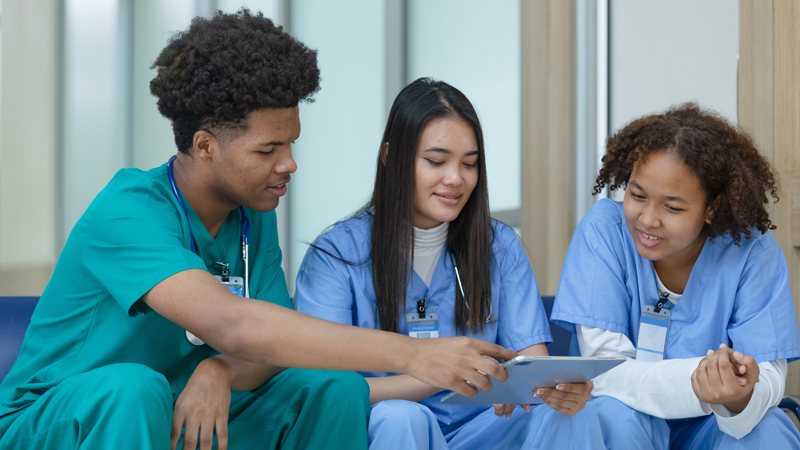 nurses in scrubs reviewing and looking at documents on a bench next to one another