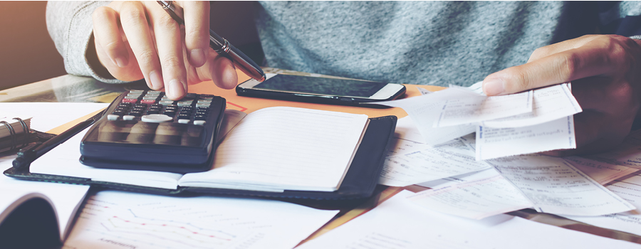 Person working on a computer desk with a calcultor and paperwork calculating expenses and financials